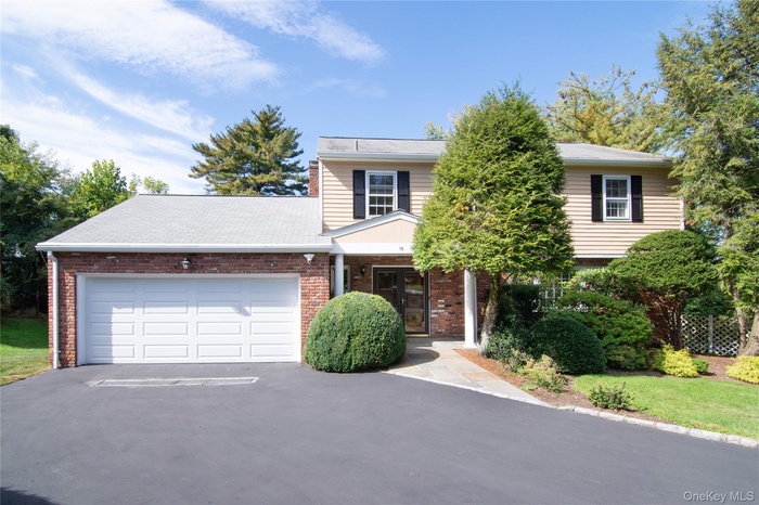 Traditional-style home featuring driveway, brick siding, an attached garage, and roof with shingles