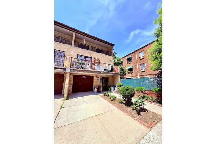 View of property featuring brick siding, concrete driveway, a balcony, and an attached garage
