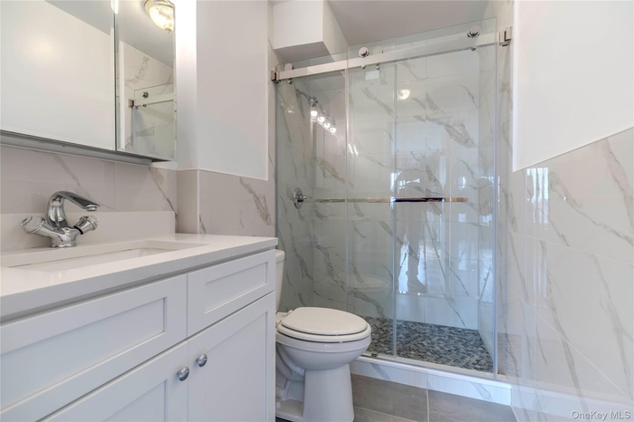 Full bathroom with a marble finish shower, vanity, tile walls, and tasteful backsplash