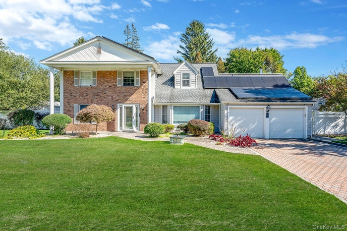 Neoclassical / greek revival house featuring a front yard, solar panels, decorative driveway, and brick siding