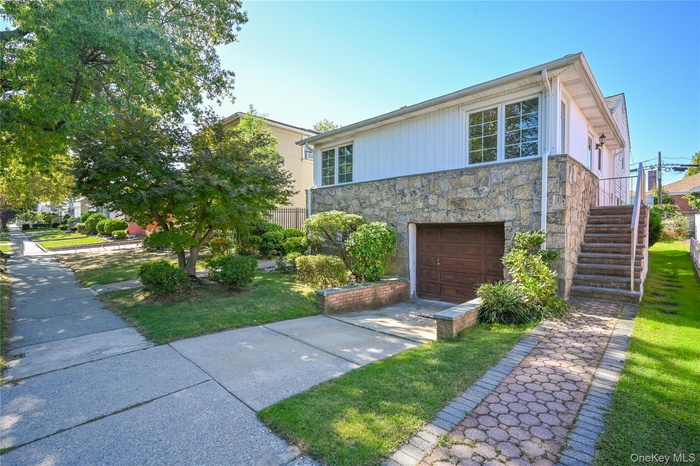 View of front of home with stairs, stone siding, driveway, an attached garage, and a front lawn