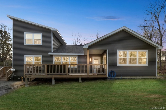 Front view of house featuring a shingled roof, a deck, and a lawn