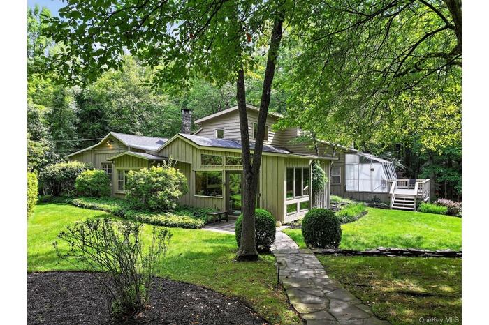 Mid-century modern home featuring a sunroom, a chimney, a front yard, board and batten siding, and a wooden deck