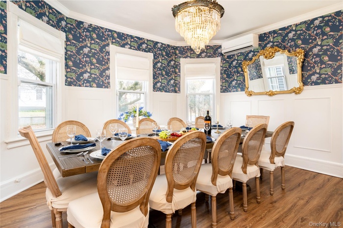 Dining room featuring wallpapered walls, a chandelier, wood finished floors, wainscoting, and crown molding
