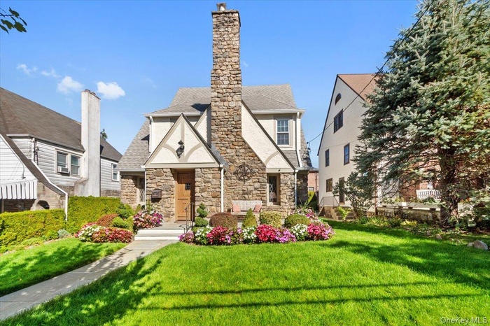 English style home with a front yard, stone siding, a chimney, and roof with shingles