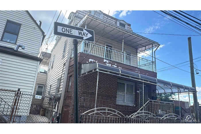 View of side of property featuring a fenced front yard, a gate, brick siding, and a balcony