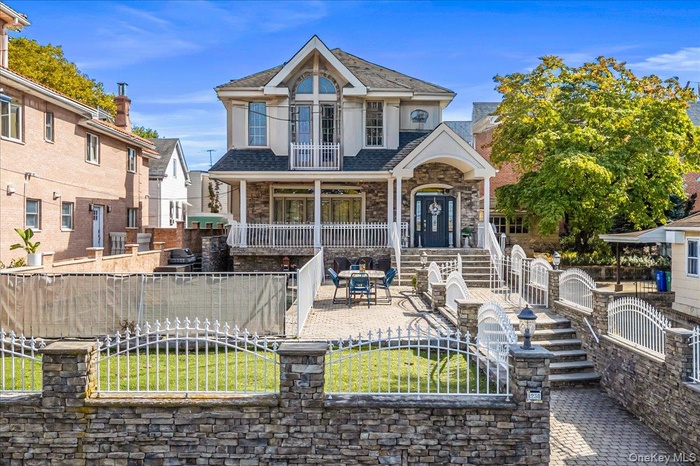 View of front of house featuring a patio, a fenced front yard, stone siding, a balcony, and a gate