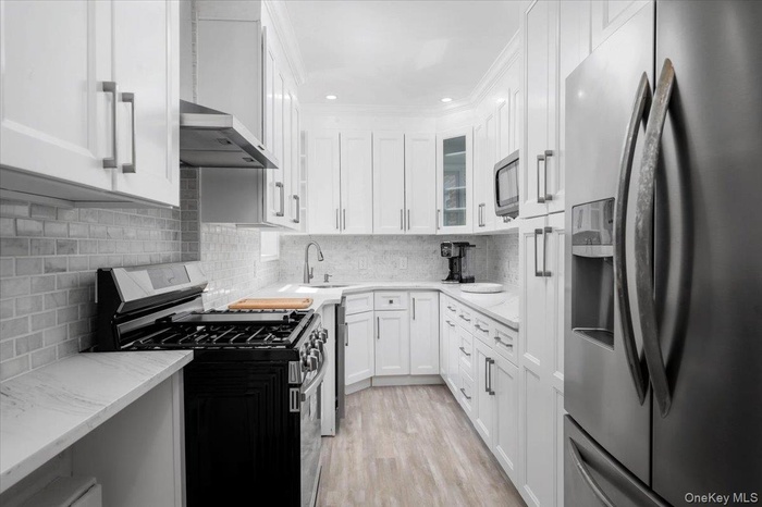 Kitchen featuring appliances with stainless steel finishes, white cabinetry, backsplash, light stone countertops, and light wood-style flooring