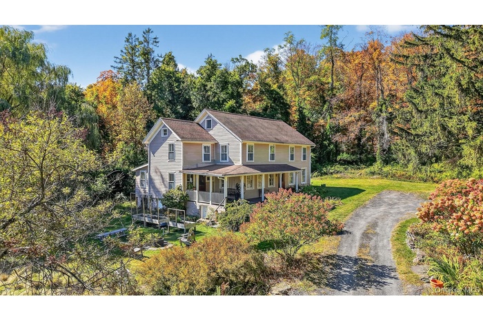 View of front of home with a porch, a front lawn, a view of trees, and asphalt driveway