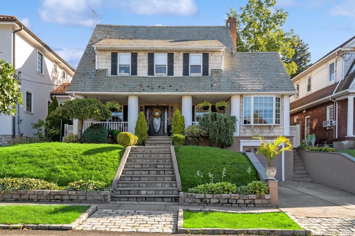 View of front of house featuring stairway, a chimney, a high end roof, an attached garage, and driveway