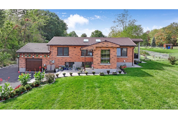 Back of house with a tile roof, a garage, brick siding, and driveway