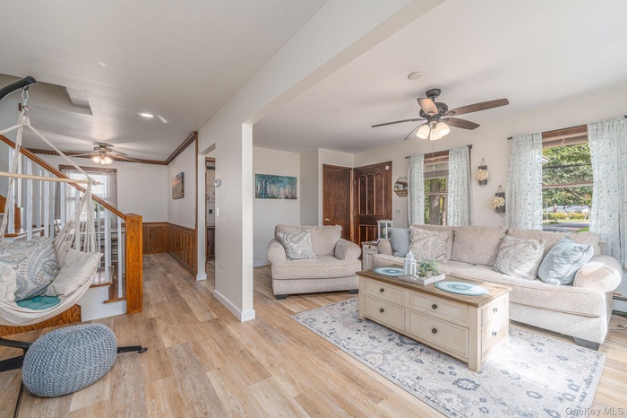 Living room featuring a ceiling fan, plenty of natural light, light wood finished floors, wainscoting, and stairway