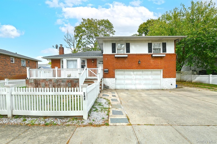 Tri-level home featuring a fenced front yard, brick siding, concrete driveway, a garage, and a wooden deck