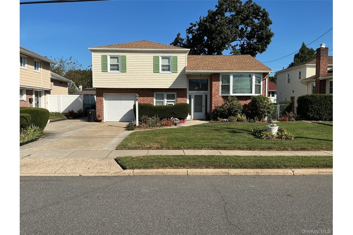 Tri-level home featuring brick siding, driveway, a shingled roof, and a garage