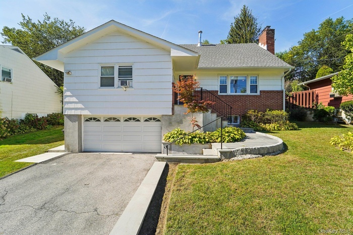 Ranch-style home featuring a front yard, a chimney, driveway, and an attached garage