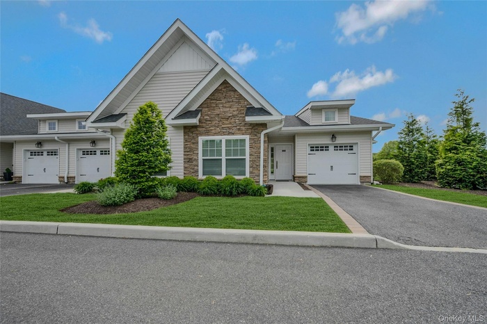 View of front of property with driveway, a front yard, and stone siding