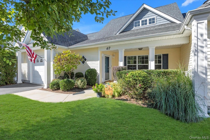 View of front facade featuring a shingled roof, an attached garage, a front lawn, driveway, and a porch