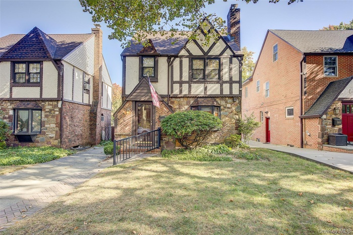 Tudor-style house featuring stucco siding, stone siding, a chimney, and a front lawn