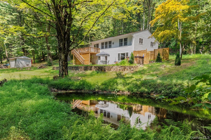 Back of property featuring stairway, a deck with water view, a view of trees, and a storage shed