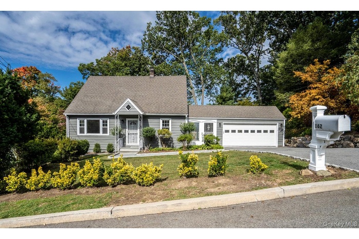 Cape cod home featuring asphalt driveway, a shingled roof, and an attached garage