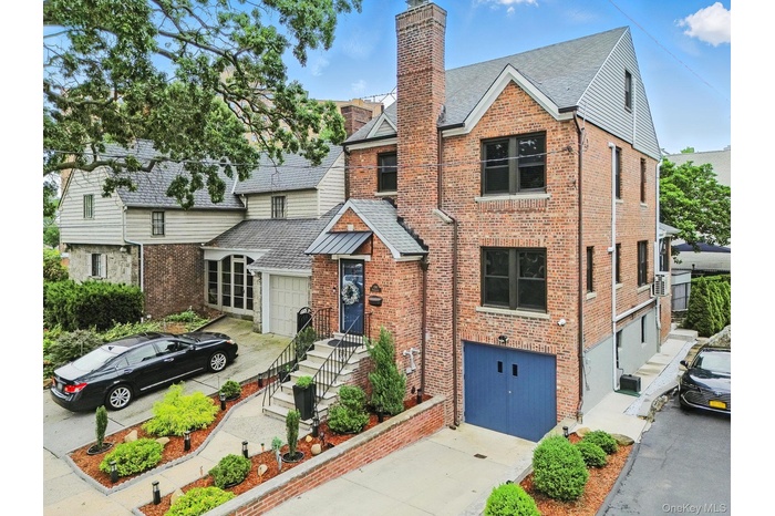 View of front facade featuring driveway, brick siding, a chimney, and a shingled roof