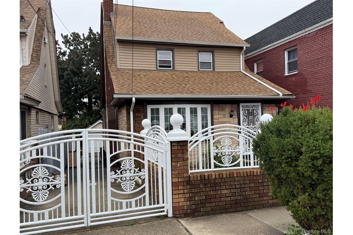 View of front facade featuring a gate, roof with shingles, a chimney, brick siding, and a fenced front yard