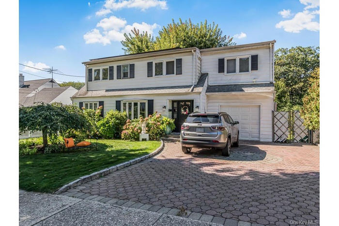 Traditional home with decorative driveway, an attached garage, and roof with shingles