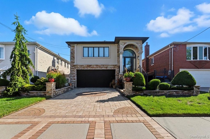 View of front facade featuring decorative driveway, stone siding, an attached garage, and a front yard
