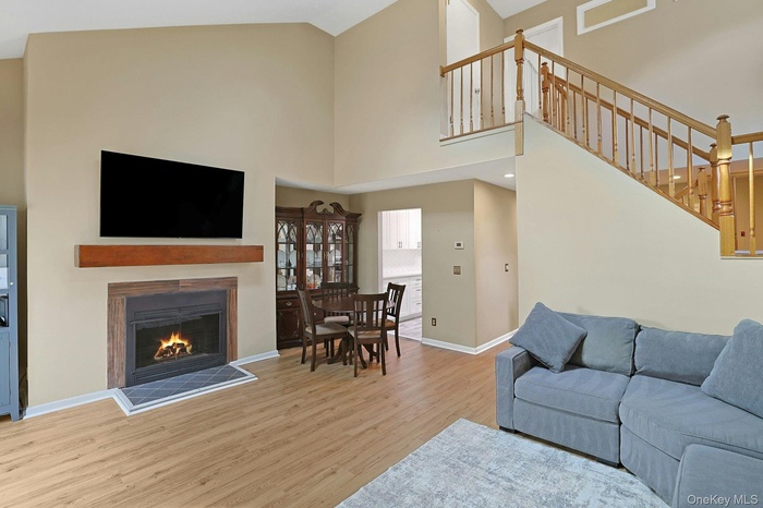 Living room featuring high vaulted ceiling, a lit fireplace, wood finished floors, and stairs