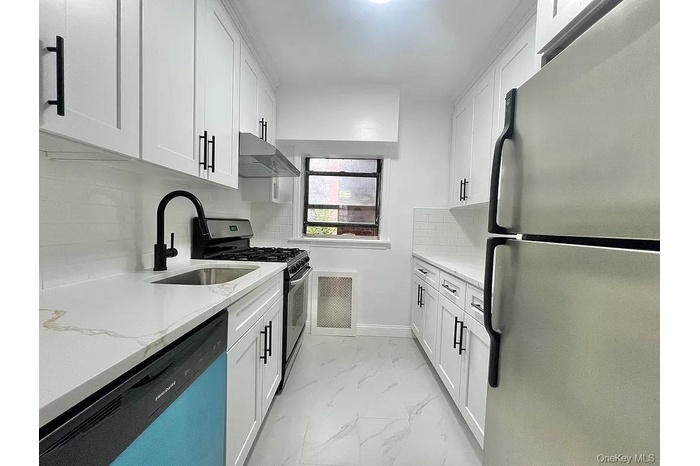 Kitchen with stainless steel appliances, light stone counters, decorative backsplash, white cabinetry, and range hood