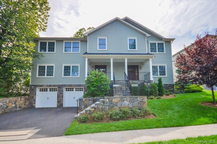 View of front facade with stairway, covered porch, stone siding, asphalt driveway, and a garage