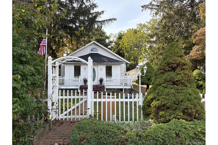 View of front of house with a gate, a fenced front yard, view of scattered trees, and a wooden deck