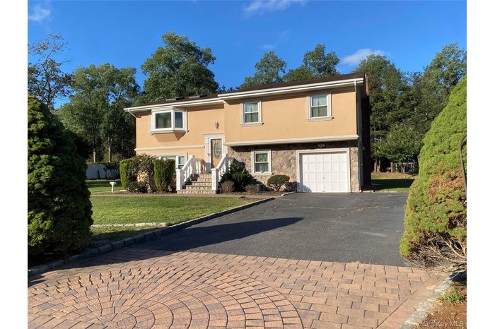 Split foyer home with stucco siding, asphalt driveway, a front lawn, stone siding, and a garage