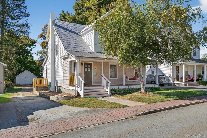 View of front of home with an outdoor structure, a porch, and roof with shingles