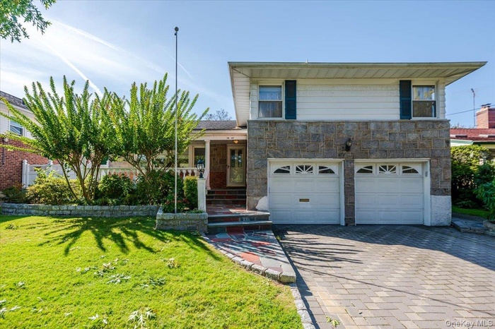 View of front facade featuring a porch, a front yard, decorative driveway, stone siding, and a garage