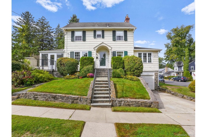 Colonial inspired home featuring a chimney, driveway, a front yard, an attached garage, and stone siding