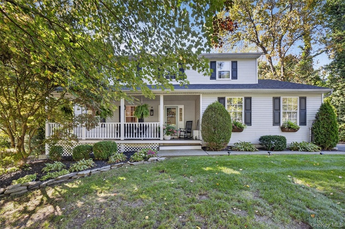 View of front of home with covered porch, a front lawn, and roof with shingles