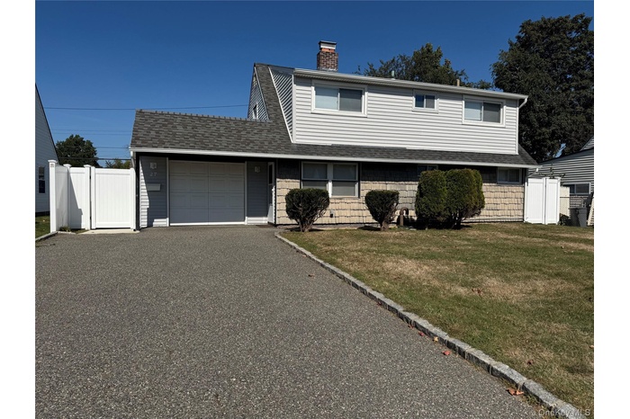 Traditional home with driveway, an attached garage, a shingled roof, a chimney, and a gate