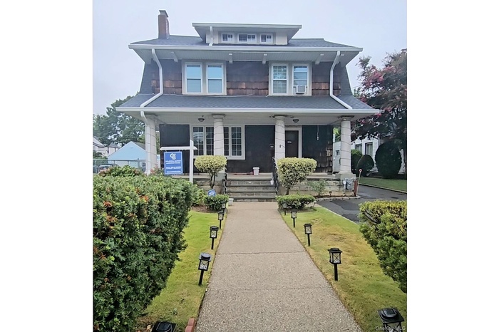 View of front of home featuring covered porch, a chimney, and a front yard