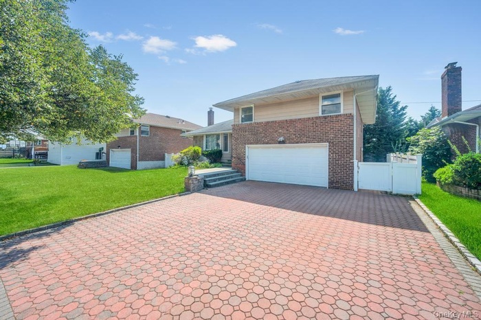 View of front of property with decorative driveway, brick siding, an attached garage, and a patio