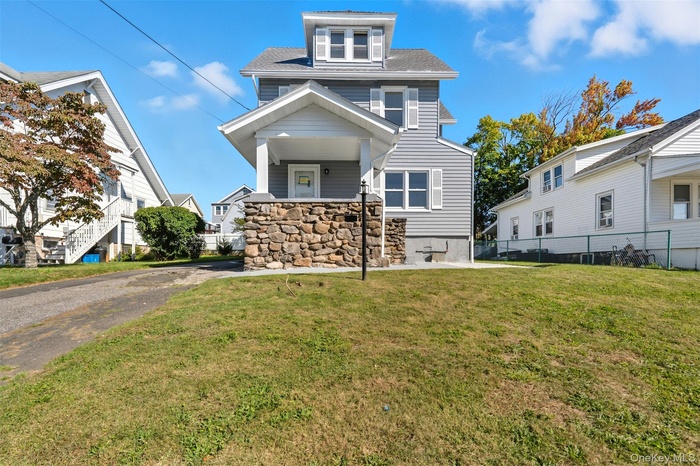 American foursquare style home with covered porch, roof with shingles, and stone siding