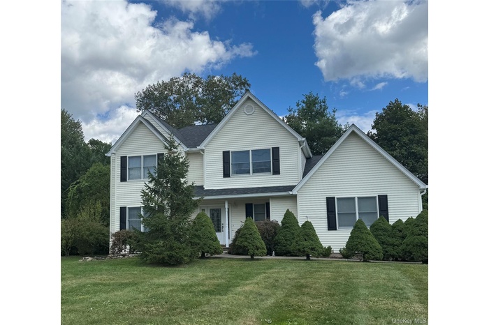 Traditional-style house with a front yard, a shingled roof, and covered porch