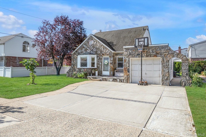 View of front of house with driveway, stone siding, and a shingled roof