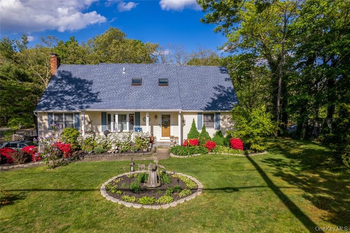 New england style home with covered porch, a front lawn, a chimney, and a shingled roof