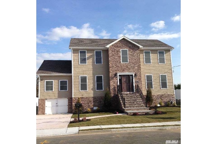 Colonial home featuring concrete driveway, stone siding, and a front lawn