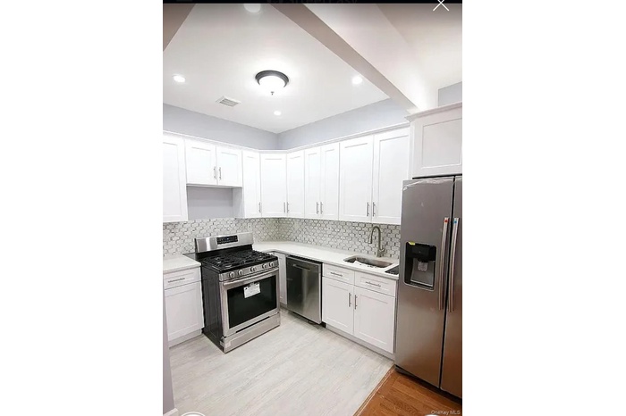 Kitchen with stainless steel appliances, tasteful backsplash, white cabinets, light wood finished floors, and recessed lighting
