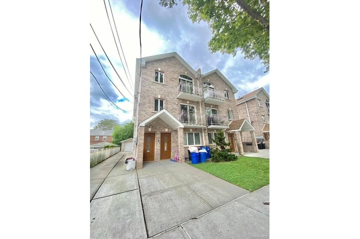 View of front of home with a balcony, brick siding, a front lawn, and an outdoor structure