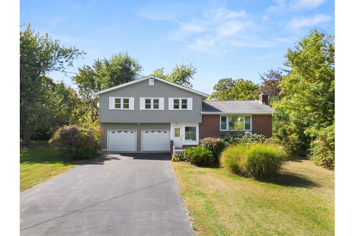 Split level home featuring driveway, a front yard, brick siding, and a chimney