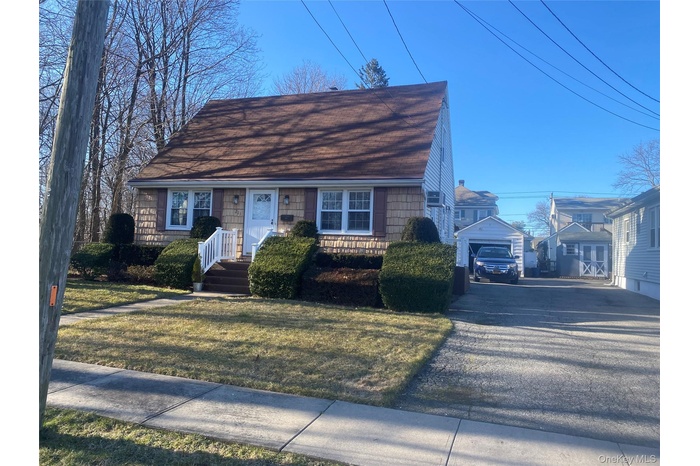 View of front of home with a shingled roof, a front yard, and an outdoor structure