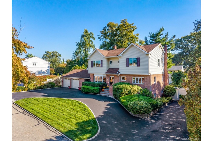 Traditional-style house featuring brick siding, driveway, an attached garage, a chimney, and a front lawn